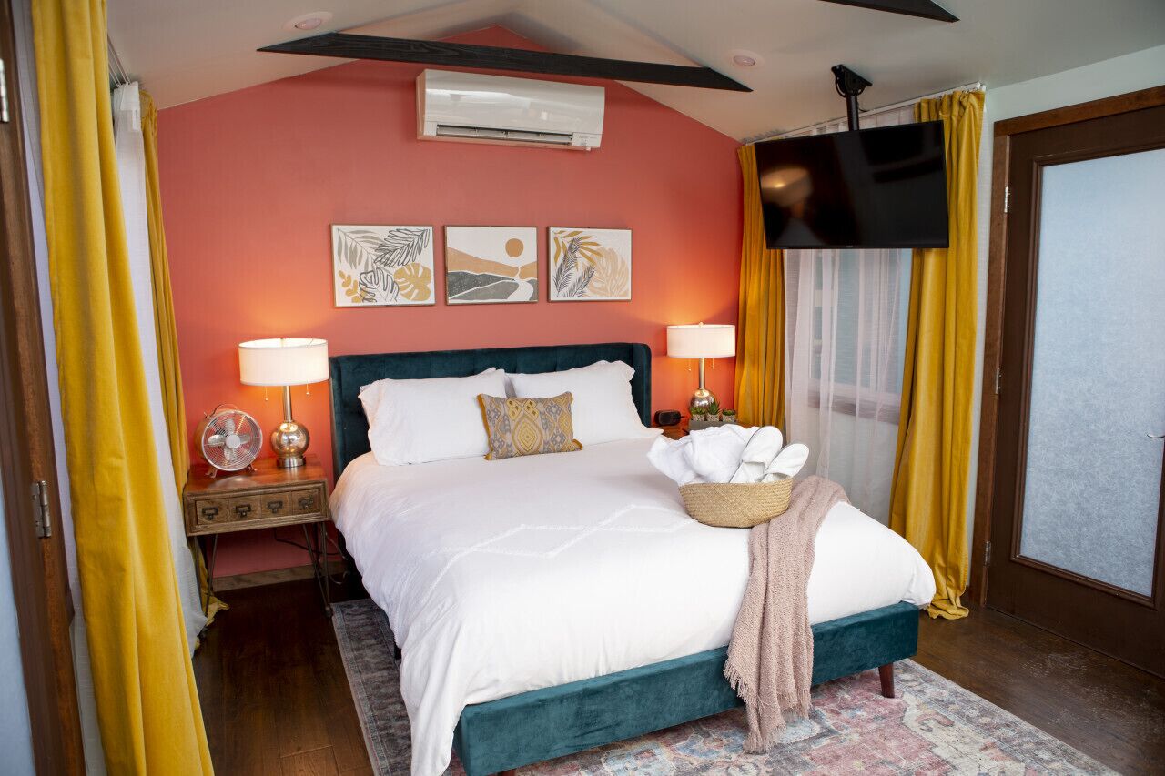 Habitació d'hotel amb un llit color turquesa, televisió de pantalla plana i obra d'art a la paret.