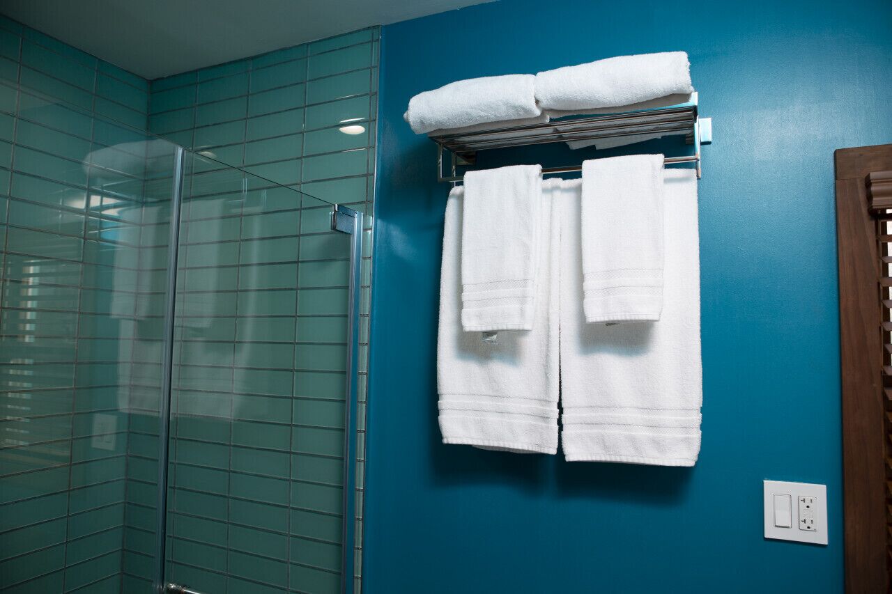 Une salle de bain aux murs de couleur turquoise, dotée d’une douche en verre et de deux serviettes blanches suspendues à un porte-serviettes.