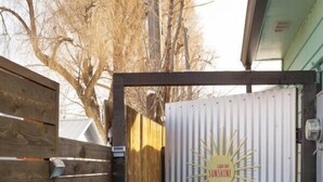 A wooden gate leading to a corrugated metal door with a sunburst design and the text "GOOD DAY SUNSHINE". - Hot Tub Studio! Sparkling Clean, Close to Oldtown. (Loveland)