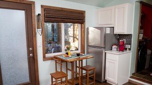 A compact kitchen with a refrigerator, a coffee maker, and a small dining area with stools. - Hot Tub Studio! Sparkling Clean, Close to Oldtown. (Loveland)