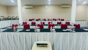 Une salle de conférence dotée de plusieurs tables, chacune étant agrémentée de chaises rouges, de bouteilles d’eau et de verres.