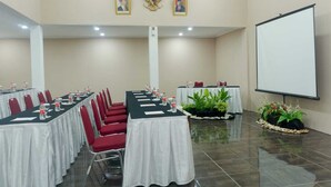 Une salle de conférence équipée de tables, de chaises, d’un écran de projection et ornée de deux portraits au mur.