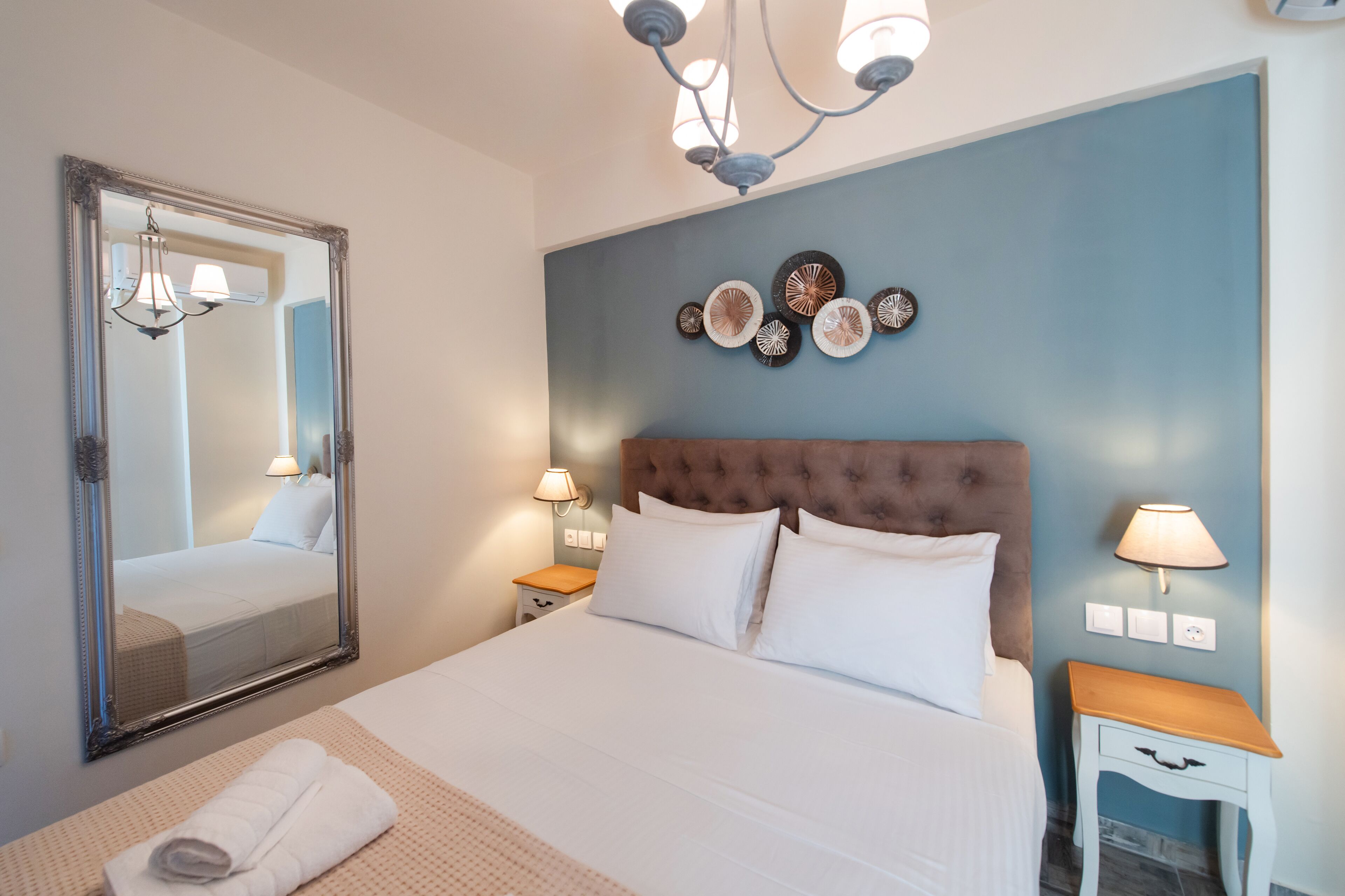 A neatly made bed with a large mirror, a tufted headboard, wall decor, and bedside lamps.