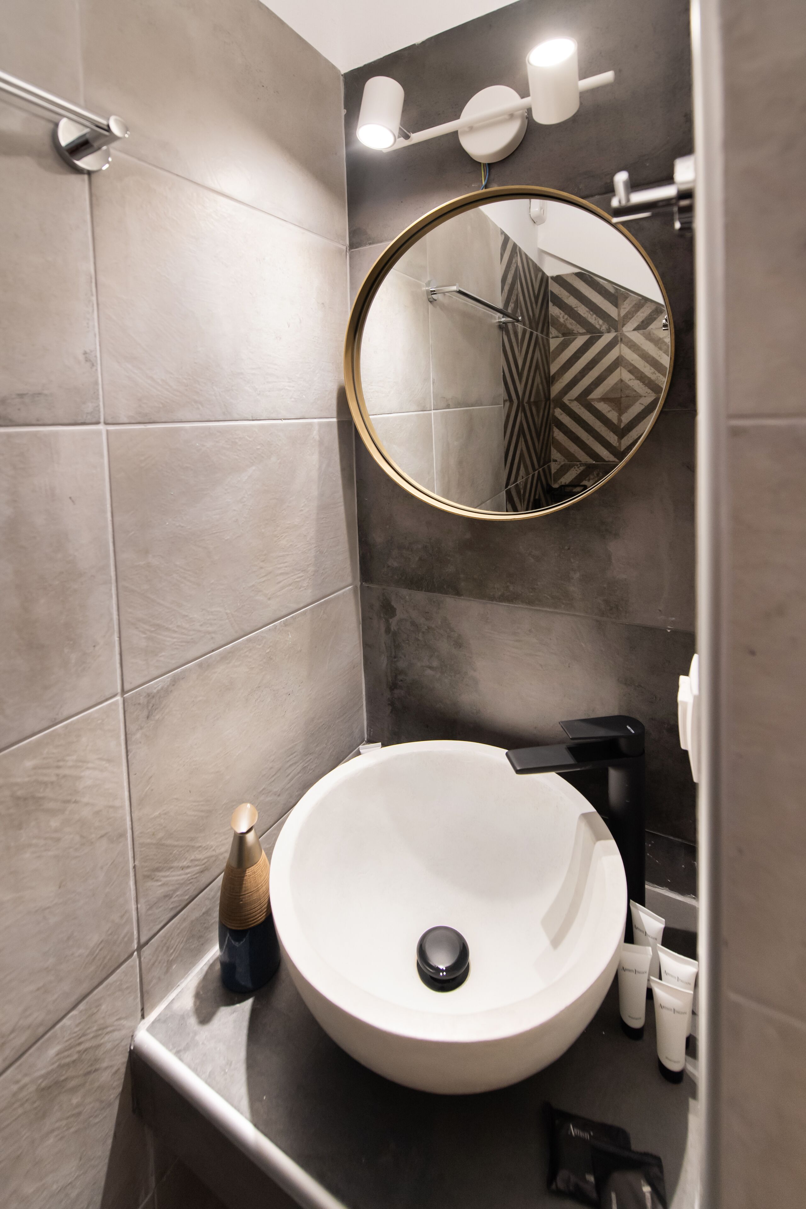 A modern bathroom with a large round sink, a handheld showerhead, and a mirror with a gold frame.
