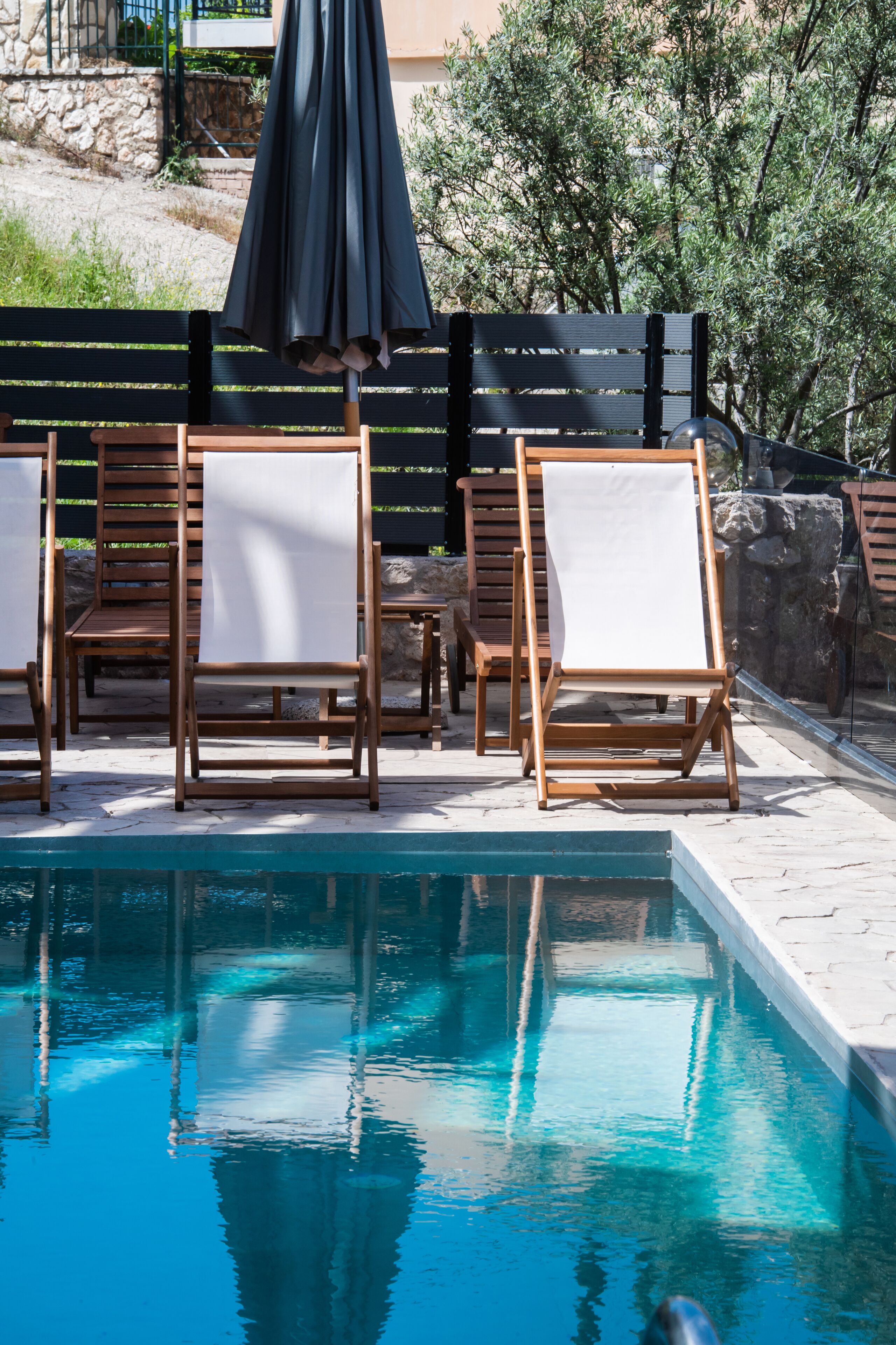Zona de piscina con sillones de madera y una sombrilla negra.