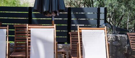 Zona de piscina con sillones de madera y una sombrilla negra.