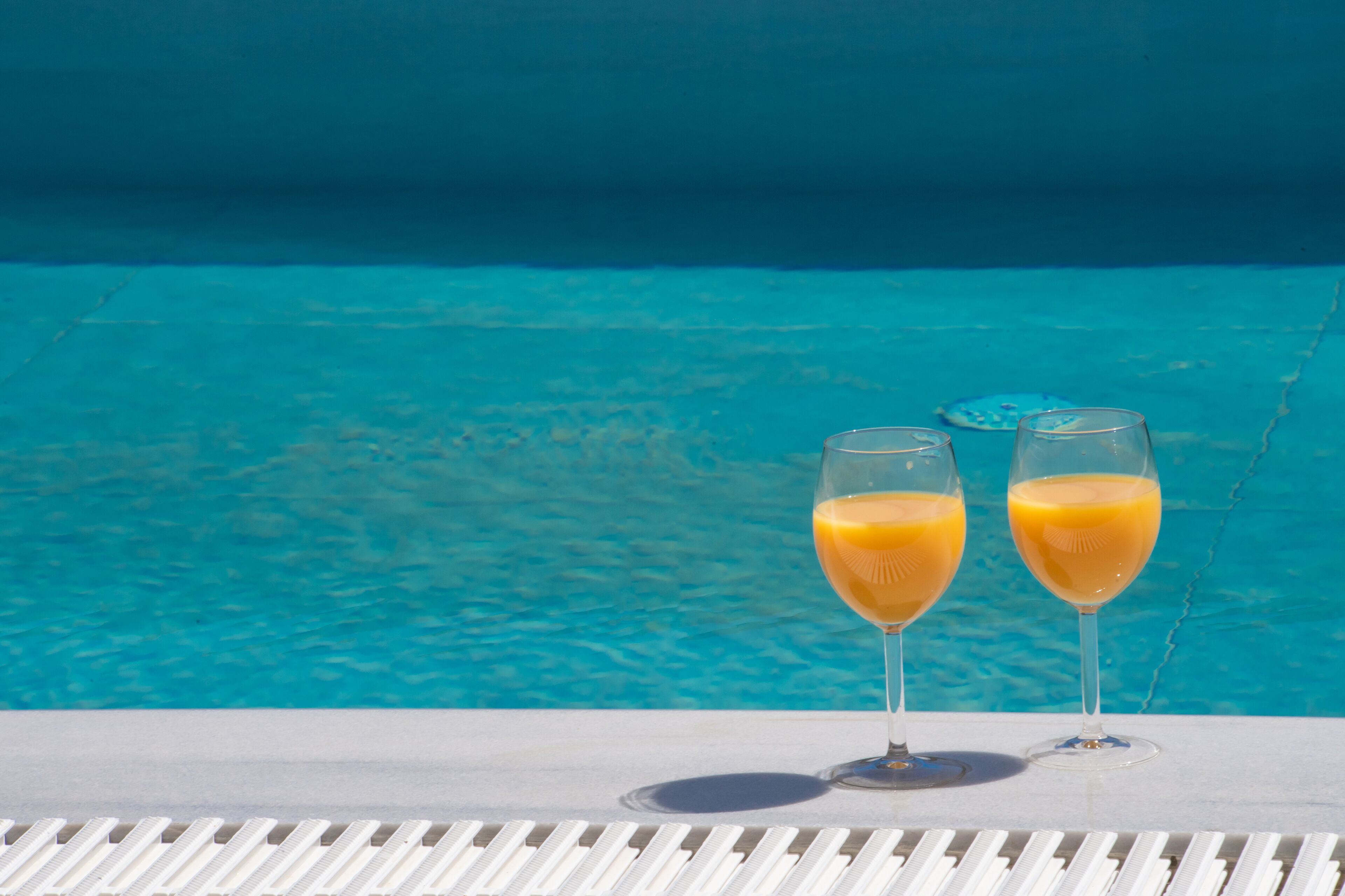 Due bicchieri di succo d'arancia su un tavolo bianco, vicino a una piscina con sfondo blu.