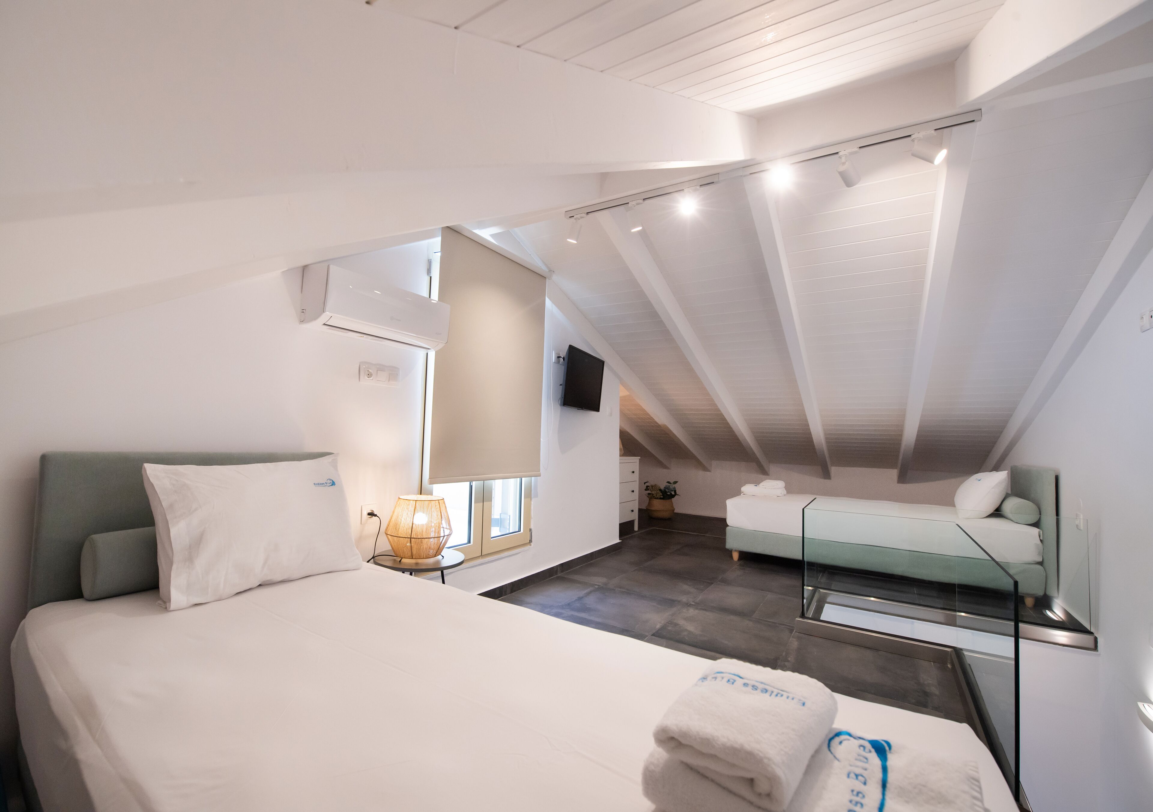 A modern hotel room with a large bed, a small desk, a chair, a bedside table, a lamp, and a flat-screen TV.