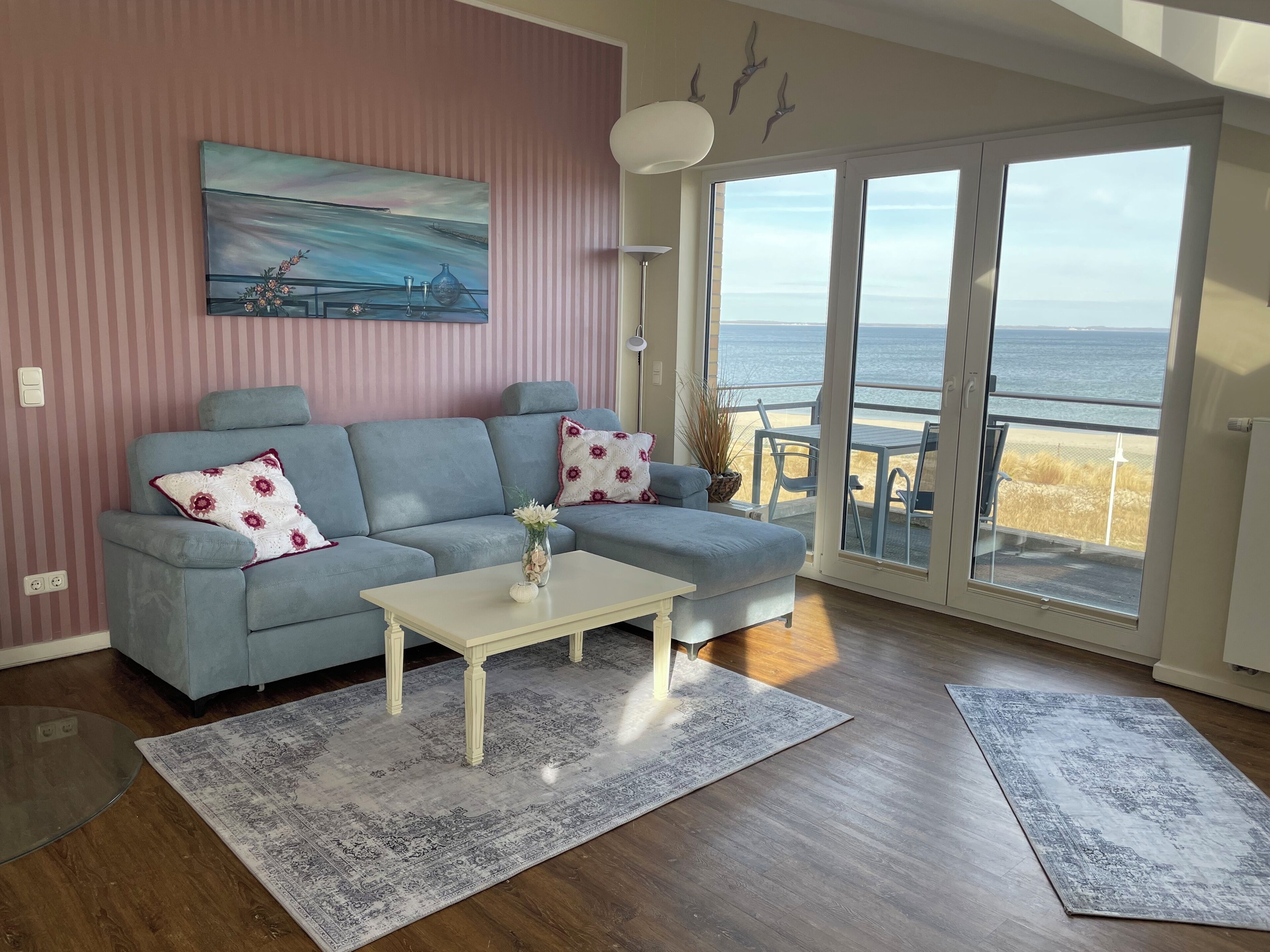 Un salon avec un canapé, une table basse et une vue sur la plage, visible à travers une porte vitrée.