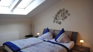 A bedroom with a bed, two bedside tables, a nightstand, a wall-mounted artwork, and a skylight.
