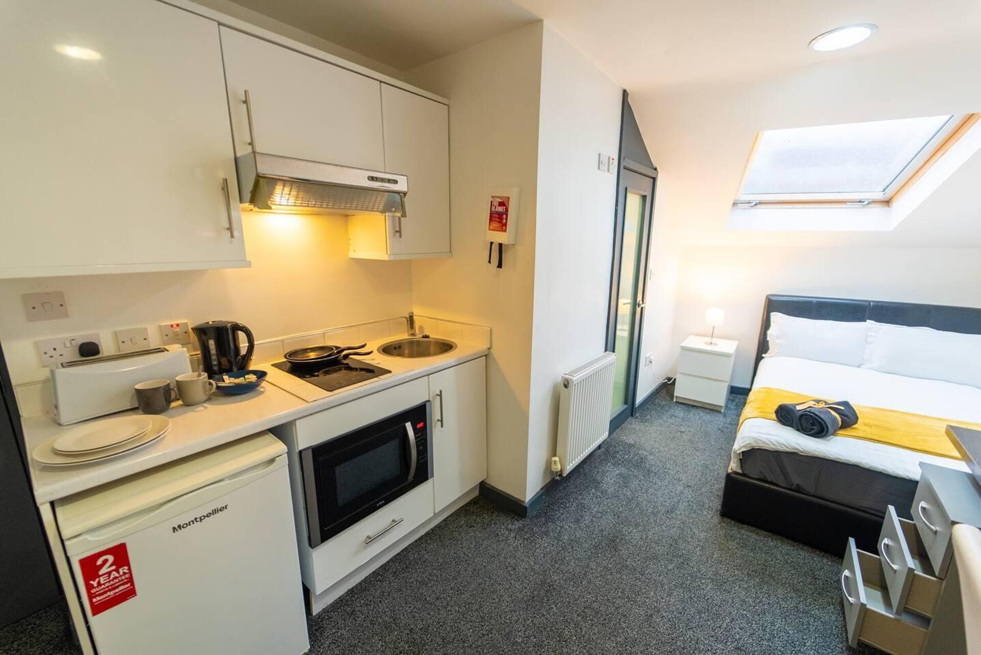 Quarto de hotel compacto com cozinha compacta, uma cama, mesa de cabeceira pequena e janela com vista.