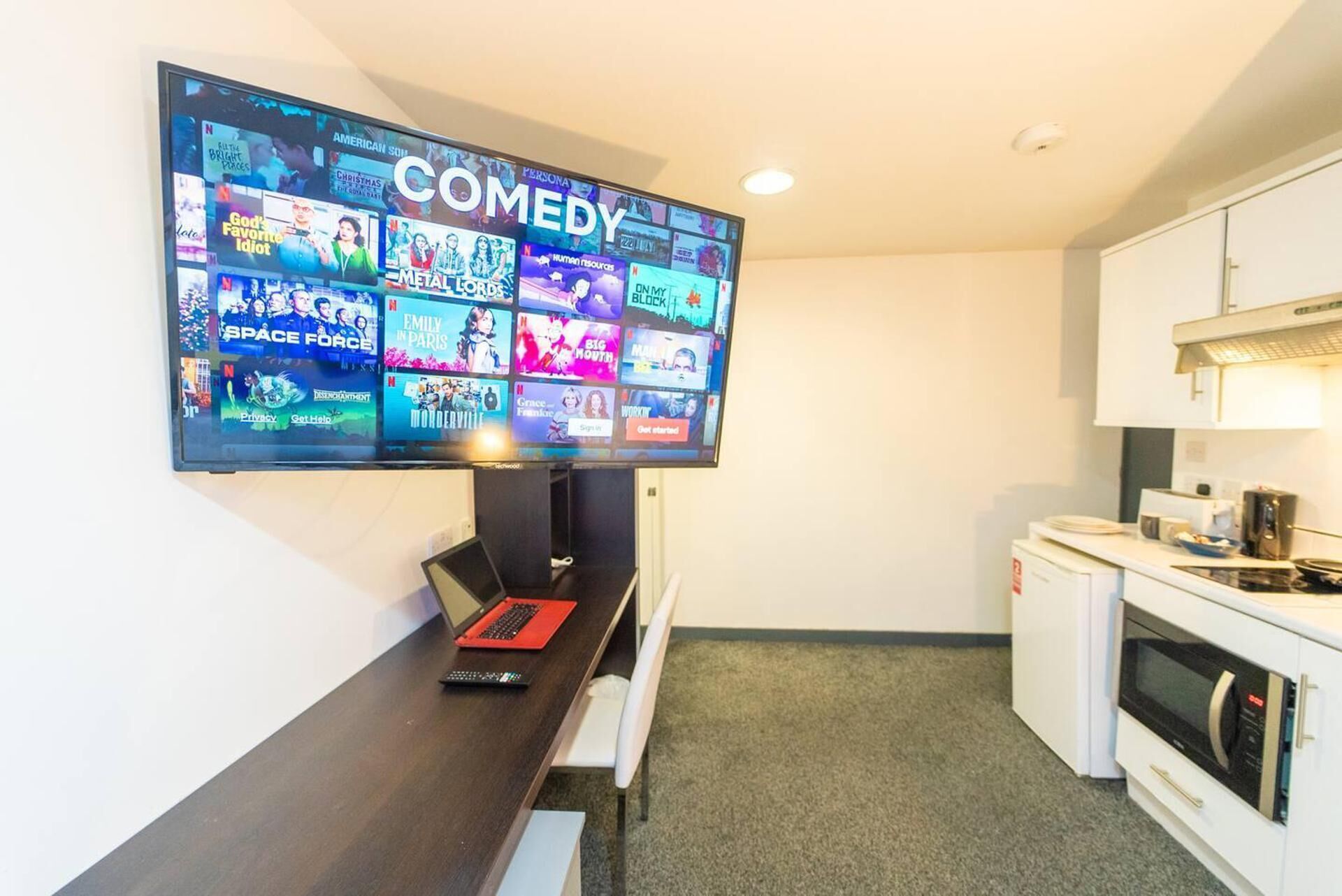 A modern kitchen with a flat-screen TV mounted on the wall displaying various comedy shows.