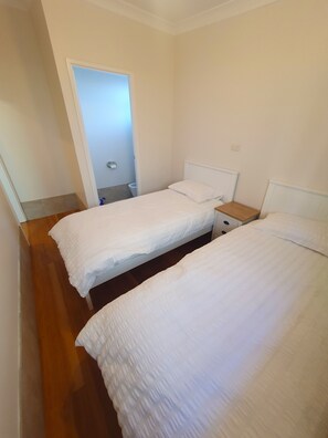 A bedroom with two single beds, a wooden floor, and a white door leading to a bathroom. - Kabine Waterfront Lakehouse in Sunshine (Sunshine)