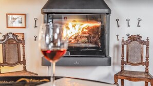 A wood-burning stove with a glass door, surrounded by antique chairs and keys on the wall. - Eighteen21 Houses - Casa dos Condes (Sousel)