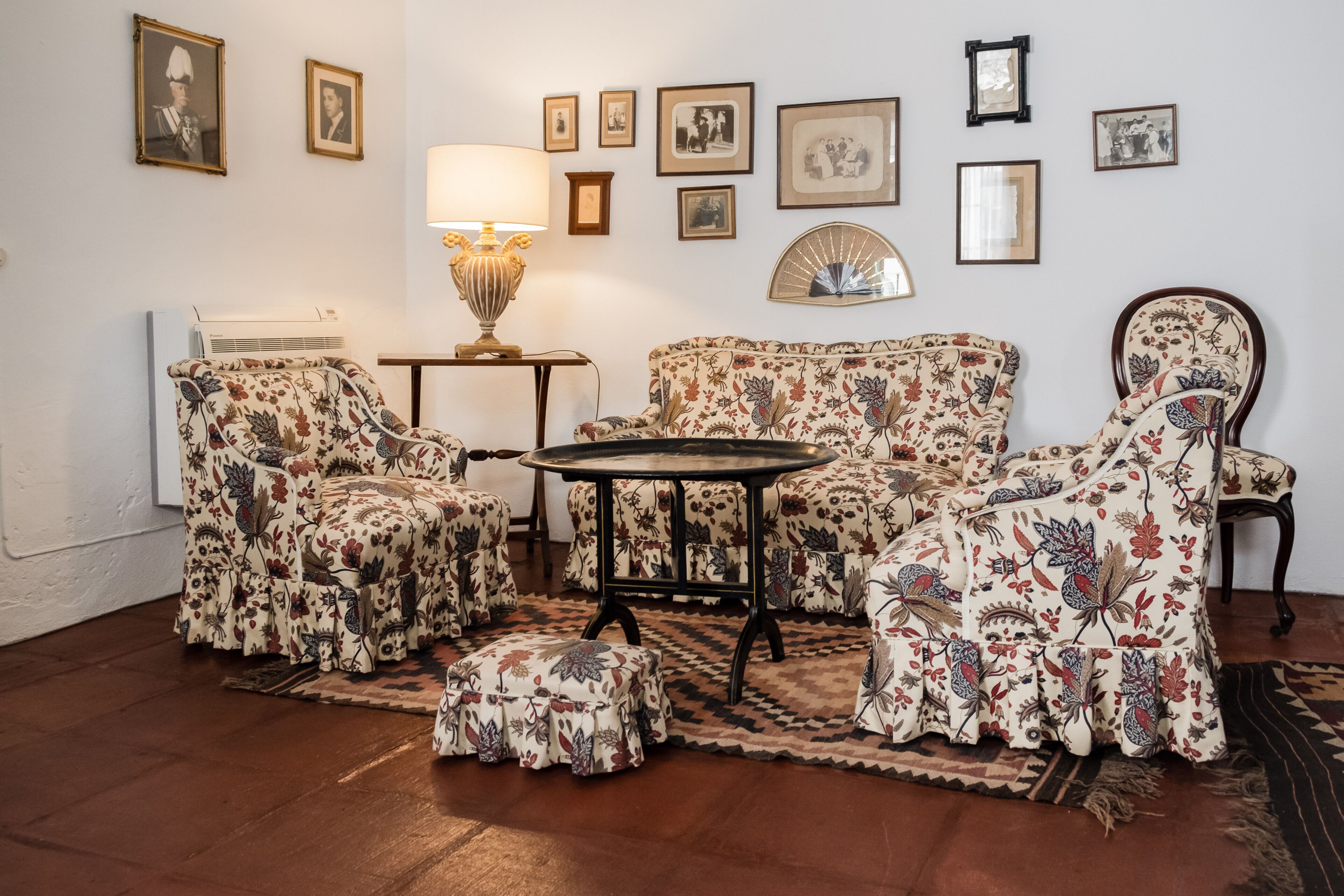 A room with floral-patterned furniture, a round table, and a radiator.