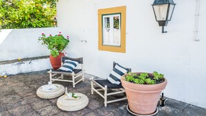 A patio with two wooden chairs, a large potted plant, and a wall-mounted lantern. - Eighteen21 Houses - Casa dos Condes (Sousel)