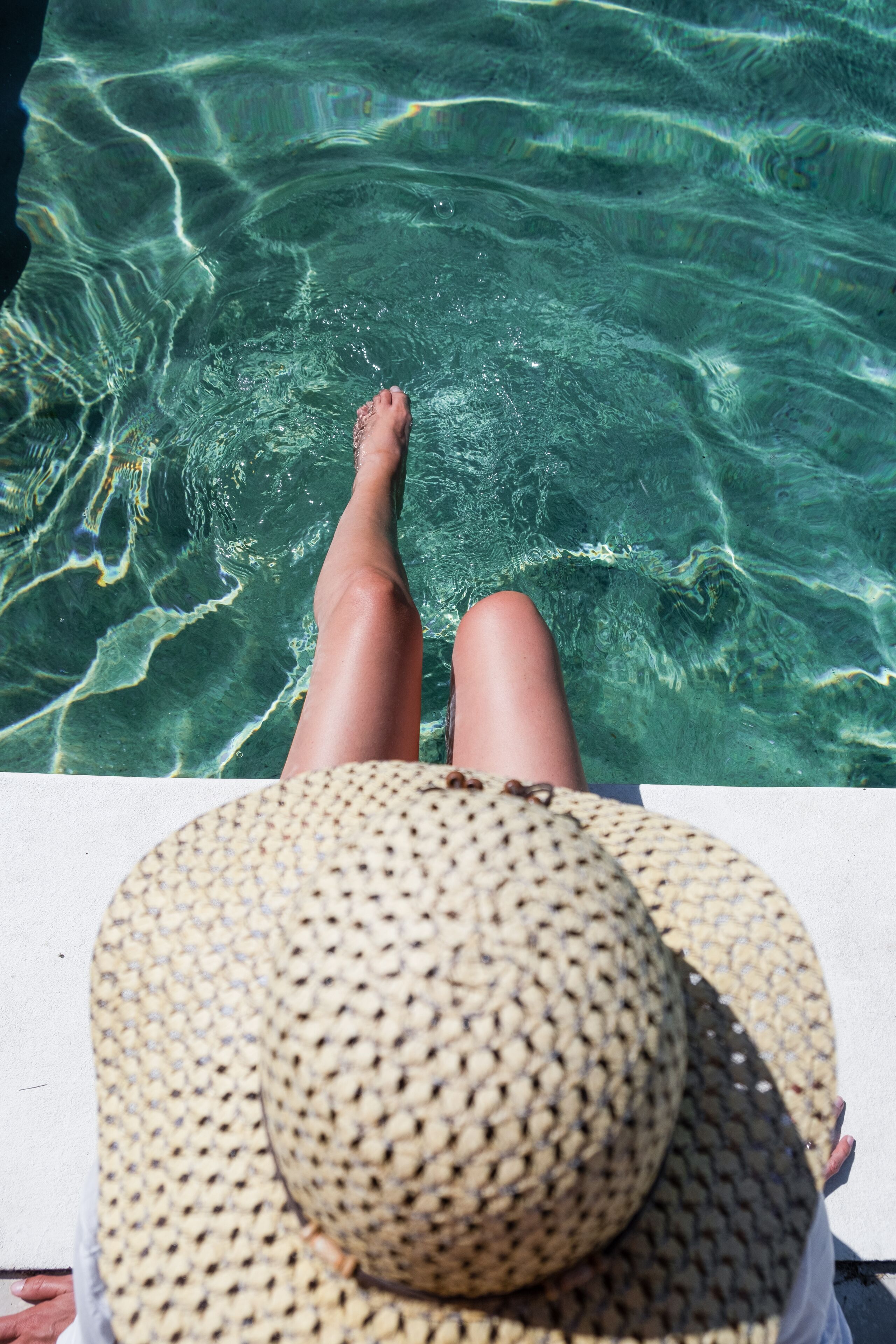 Eine Person entspannt am Pool, mit einem breitkrempigen Hut.