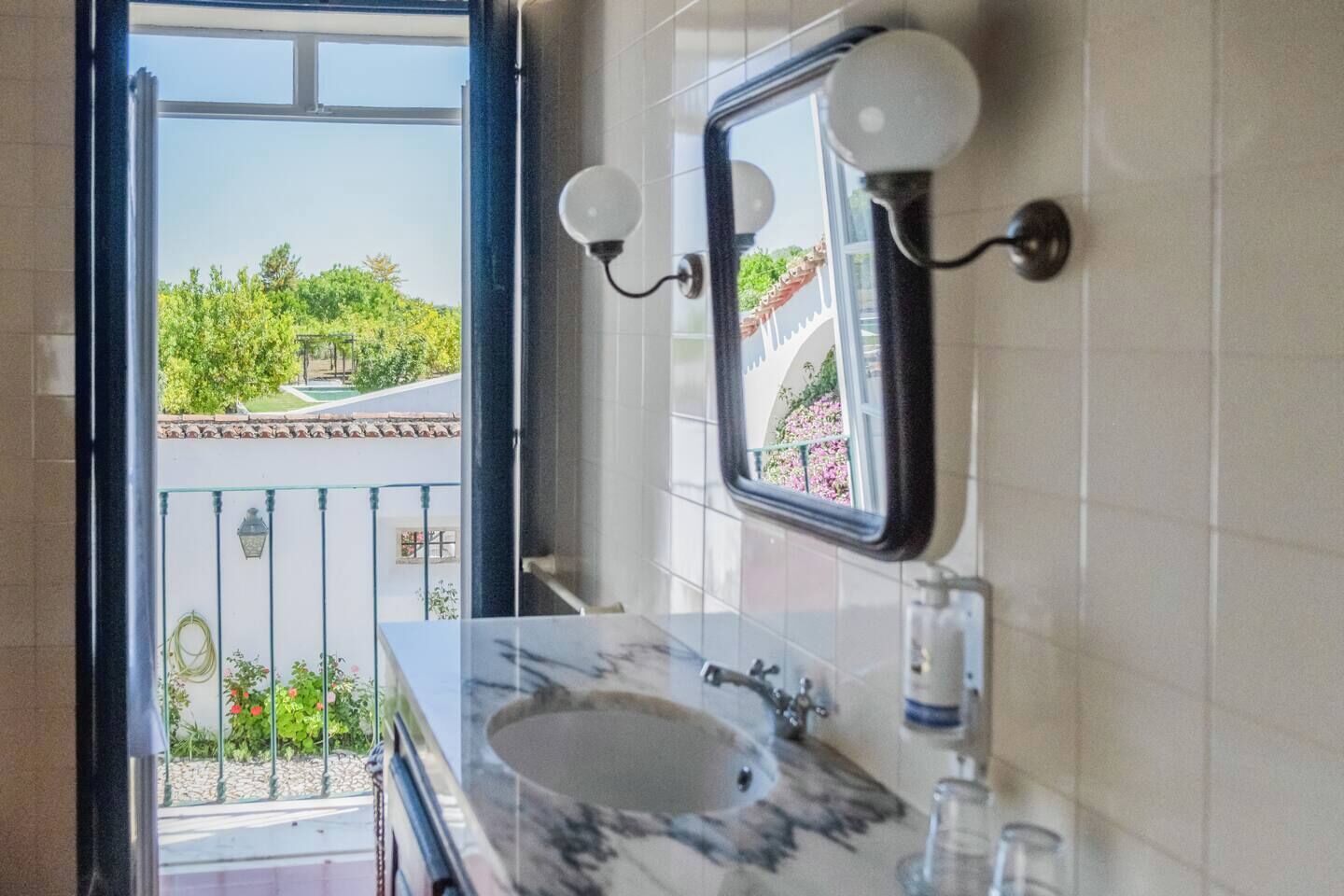 Ein Badezimmer mit Marmorwaschtisch, einem Spiegel und Blick auf einen Balkon mit Grünpflanzen und einem Gebäude.