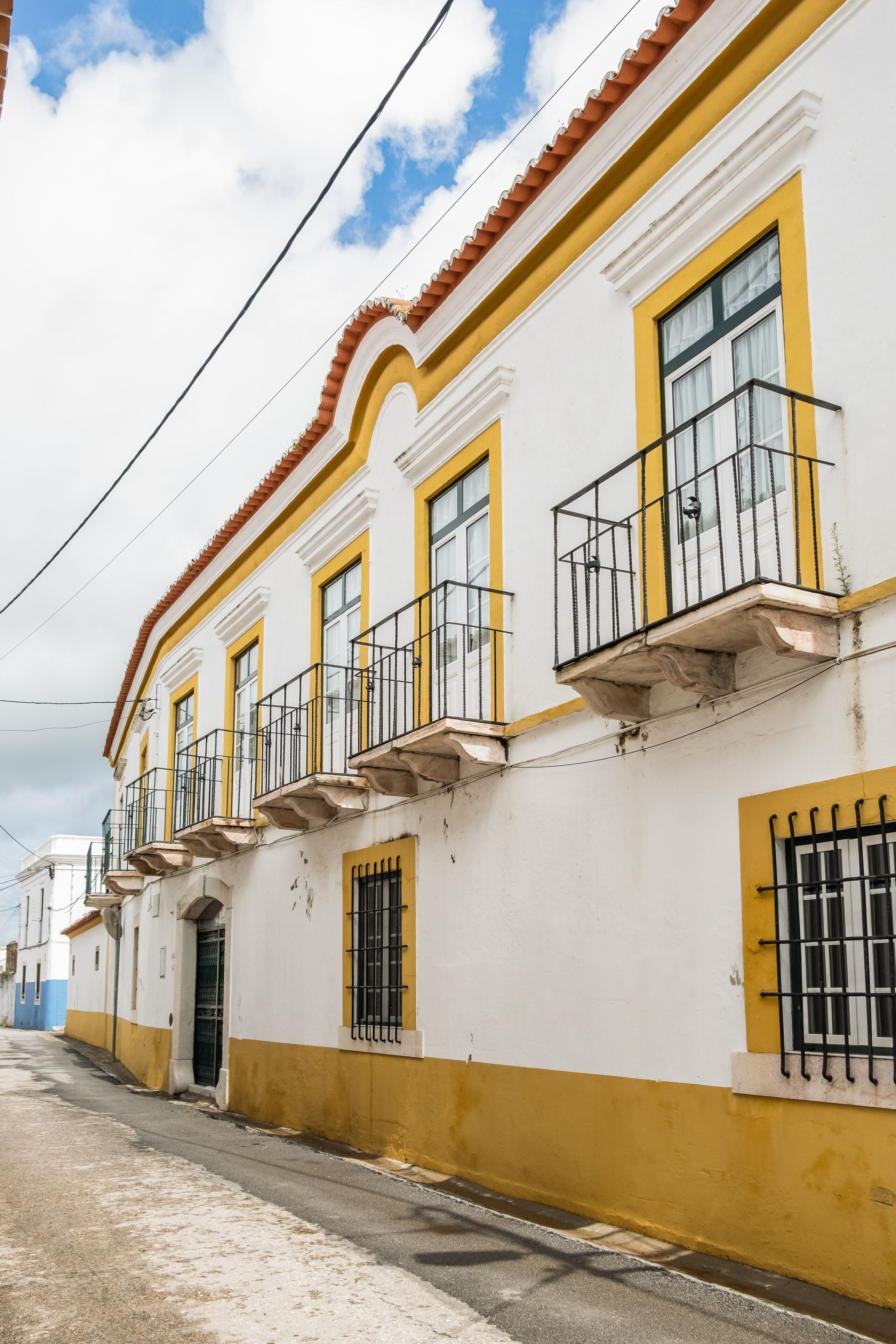 Un edificio con paredes exteriores amarillas y blancas, varios balcones y una calle en primer plano.