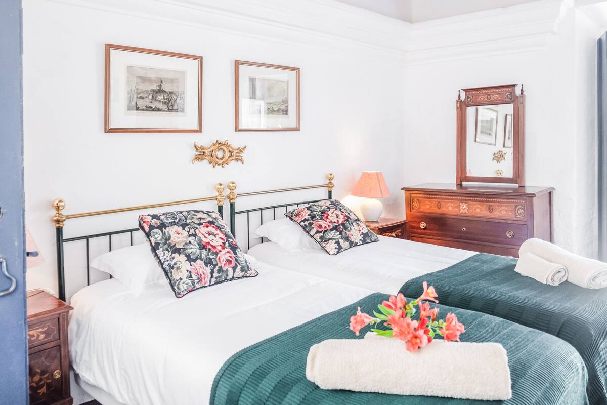 A hotel room with two beds, a dresser, a mirror, and framed pictures on the wall.