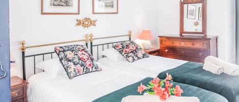 A hotel room with two beds, a dresser, a mirror, and framed pictures on the wall.
