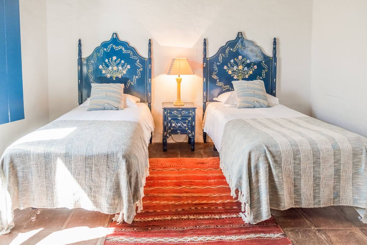A room with two beds, a nightstand with a lamp, and a red carpet.