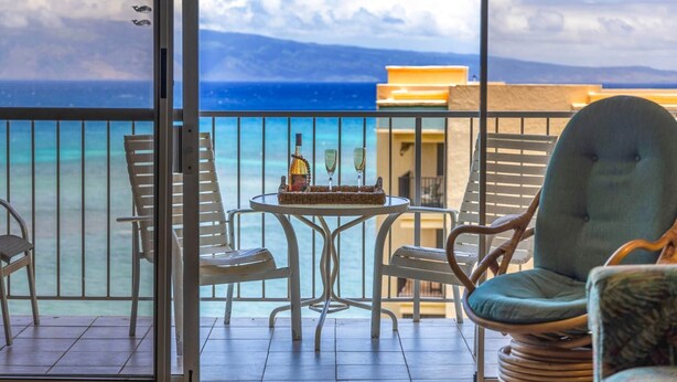A balcony with a table, chairs, and a bottle of wine.