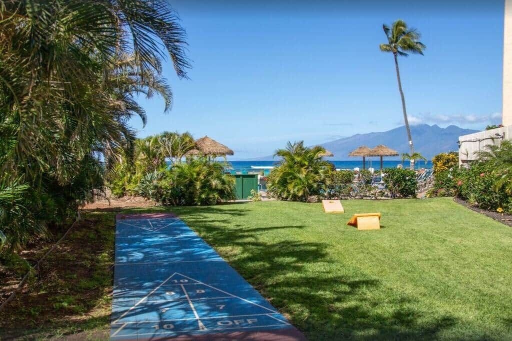Een tuin met een jeu de boules baan, palmbomen en uitzicht op de oceaan.