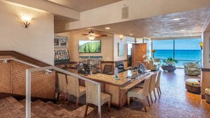 A spacious room with a large desk, chairs, a television, and a view of the ocean.