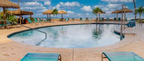 A pool with lounge chairs and thatched umbrellas.