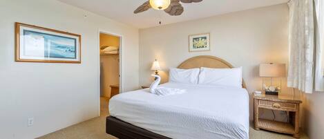 Habitación de hotel con cama, ventilador de techo, mesita de noche, lámpara y un cuadro en la pared.