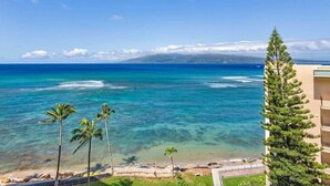 A coastal view with a clear sky, a beach, and a building with balconies overlooking the ocean.
