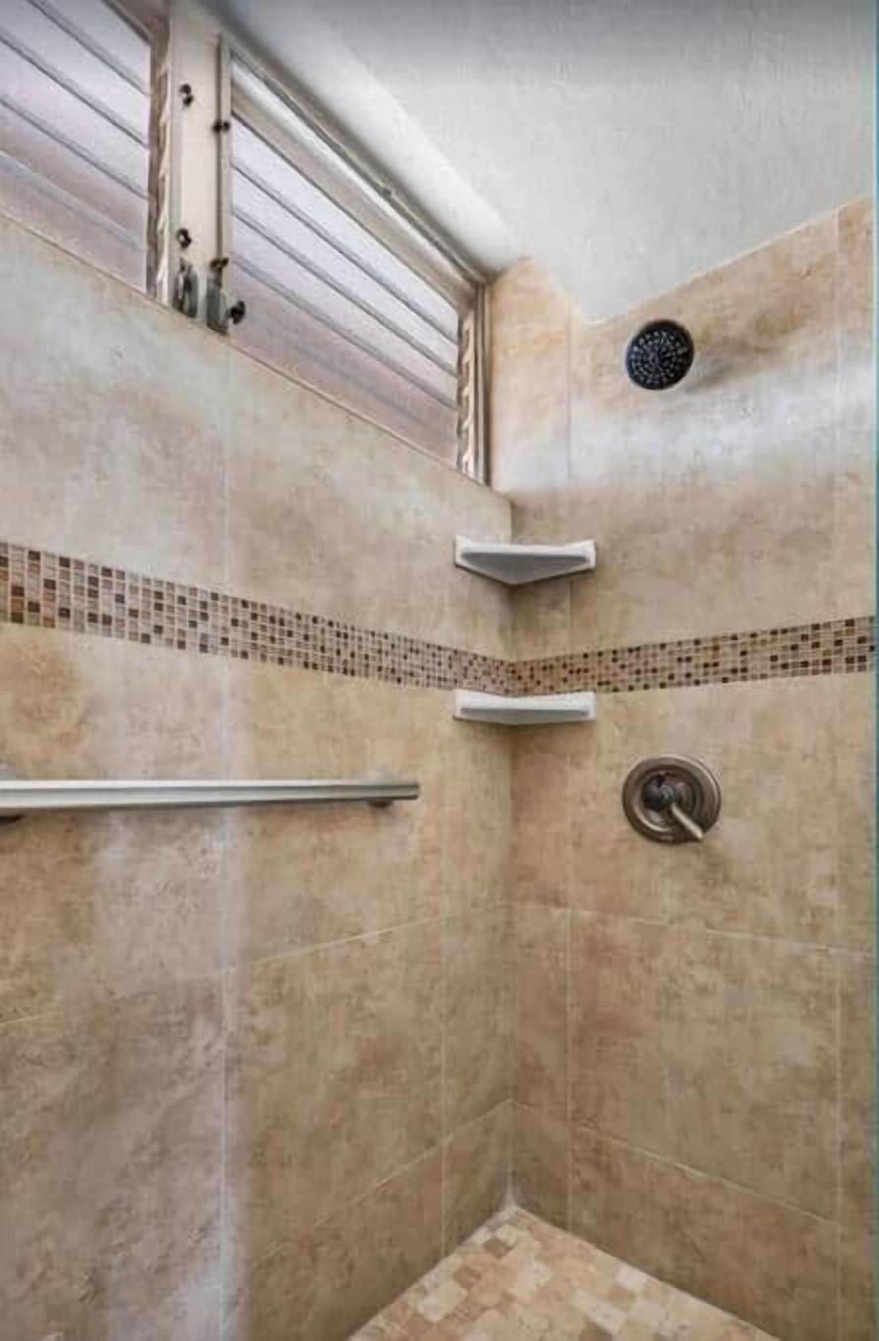 Una ducha con pared de azulejos, un pasamanos metálico y un panel de control.