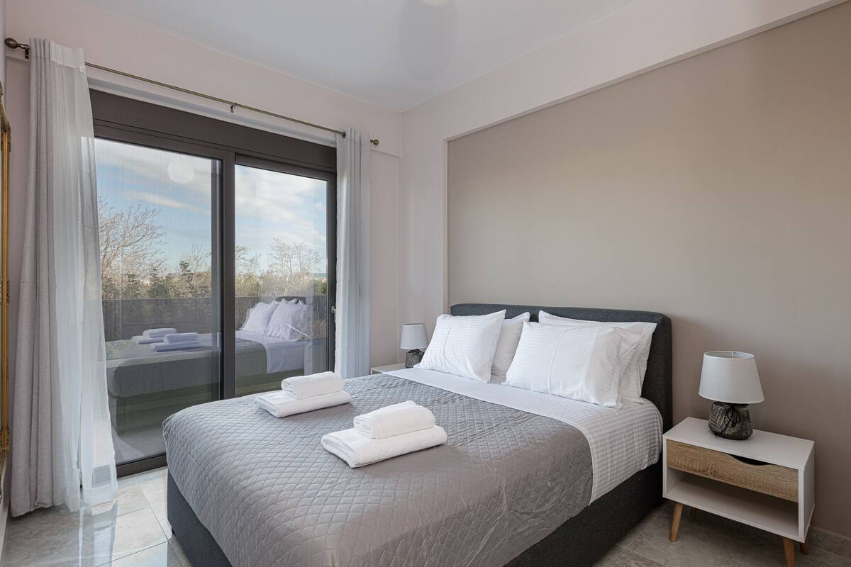 A modern bedroom with a large bed, a nightstand, and a view through a sliding glass door.