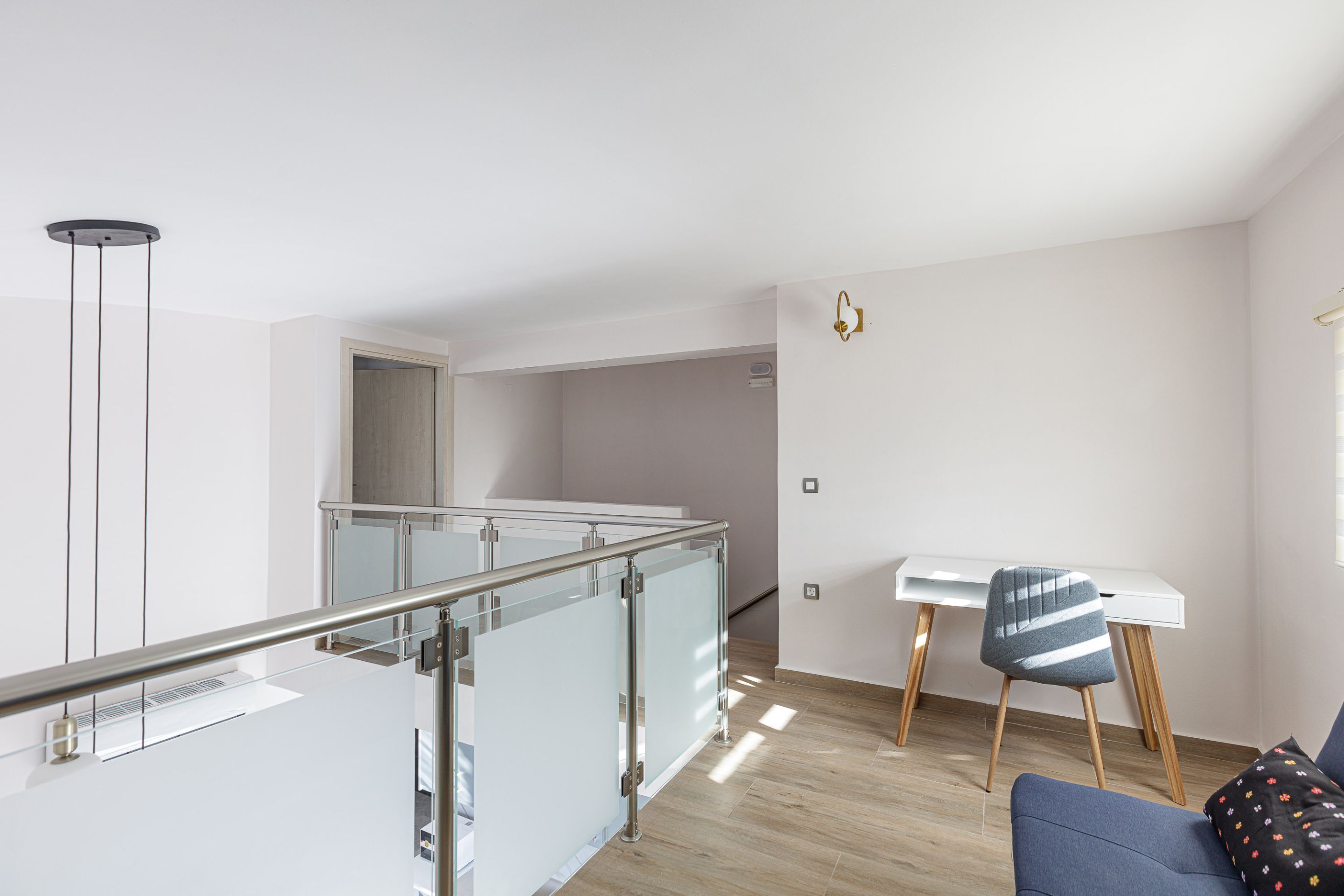 A modern apartment with a glass railing, a dining area with a white table and chairs, and a blue sofa with a patterned pillow.