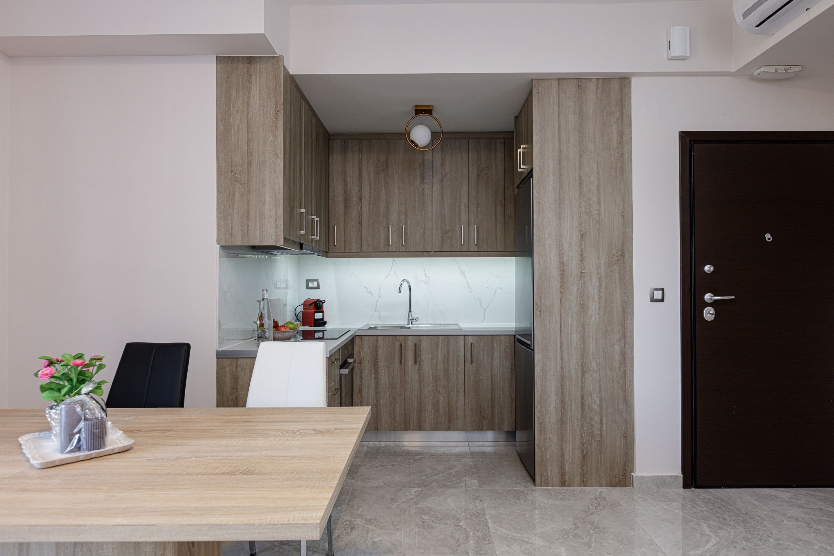 A modern kitchen with wooden cabinets, a marble countertop, and a black door.