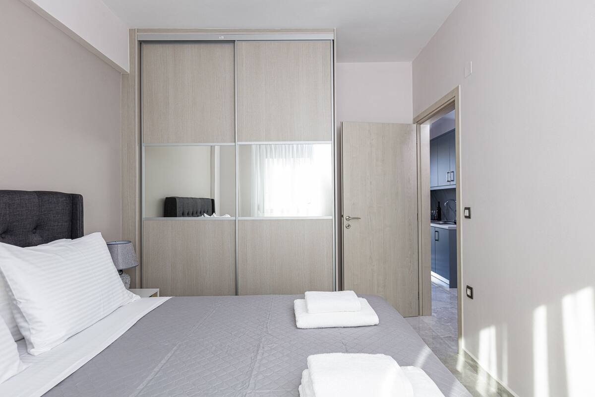 A modern hotel room with a large bed, a wardrobe, and a view of the kitchen.