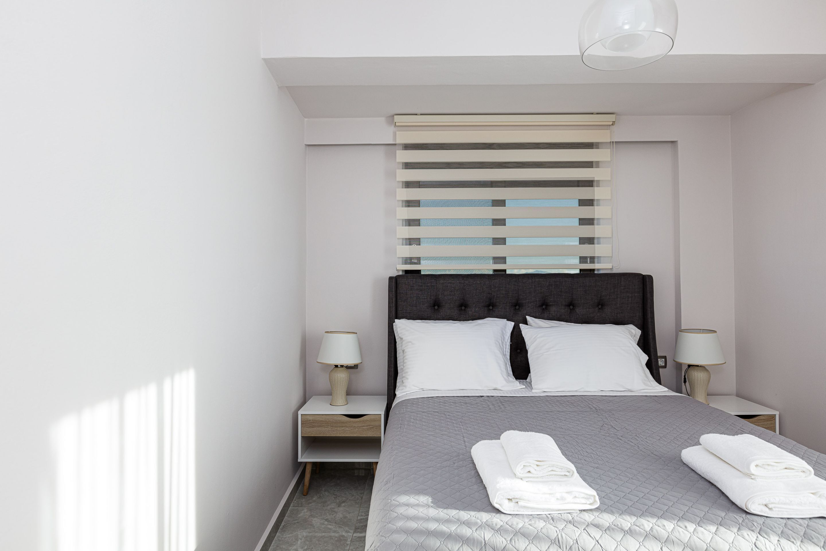 Una habitación de hotel moderna con una cama grande, dos mesitas de noche con lámparas y una ventana con persianas.