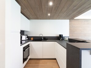 Een moderne keuken met witte kasten, een zwart aanrecht, een houten plafond en een inbouwoven.
