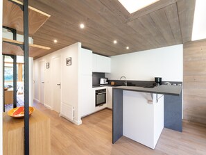 A modern kitchen with white cabinets, a black countertop, and wooden flooring. - Renovated apartment near slopes with Wi-Fi for families (Courchevel)