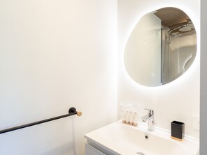 Une salle de bain avec un miroir rond, un lavabo blanc et un porte-serviettes noir.
