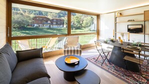 A modern living room with a large window, a sofa, a coffee table, and a dining area with a TV. - Renovated apartment near slopes with Wi-Fi for families (Courchevel)