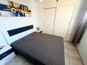 Une chambre à coucher comprenant un lit, une table de chevet, une lampe, un tableau ou une décoration murale, et une armoire.