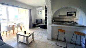 A compact living space with a dining area, a TV, a kitchenette, and a large window. - Comfortable apartment, 50m from beach, 4 people, terrace, TV, washing machine (Roses)
