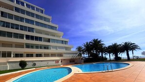 A modern hotel with a pool area, palm trees, and a clear blue sky.