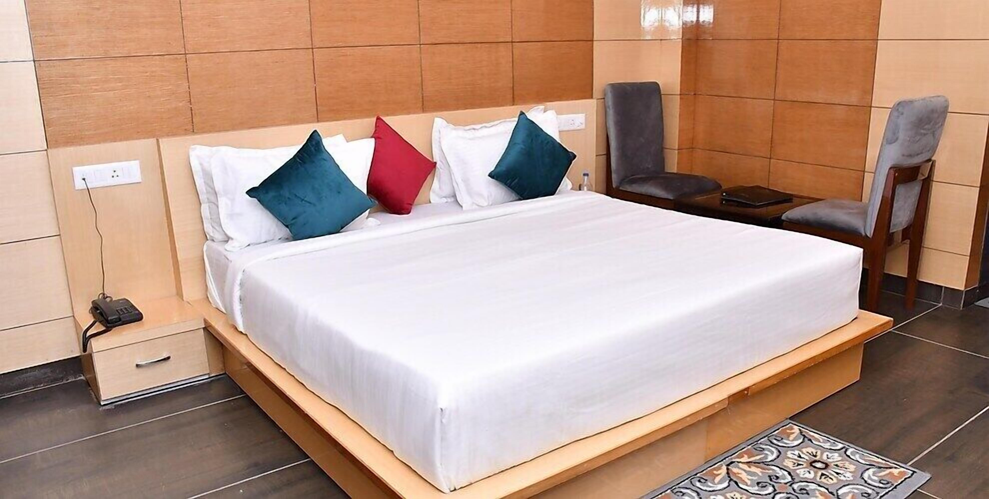 Une chambre d’hôtel équipée d’un lit, d’oreillers, d’une chaise, d’une table de chevet et d’une prise de courant.