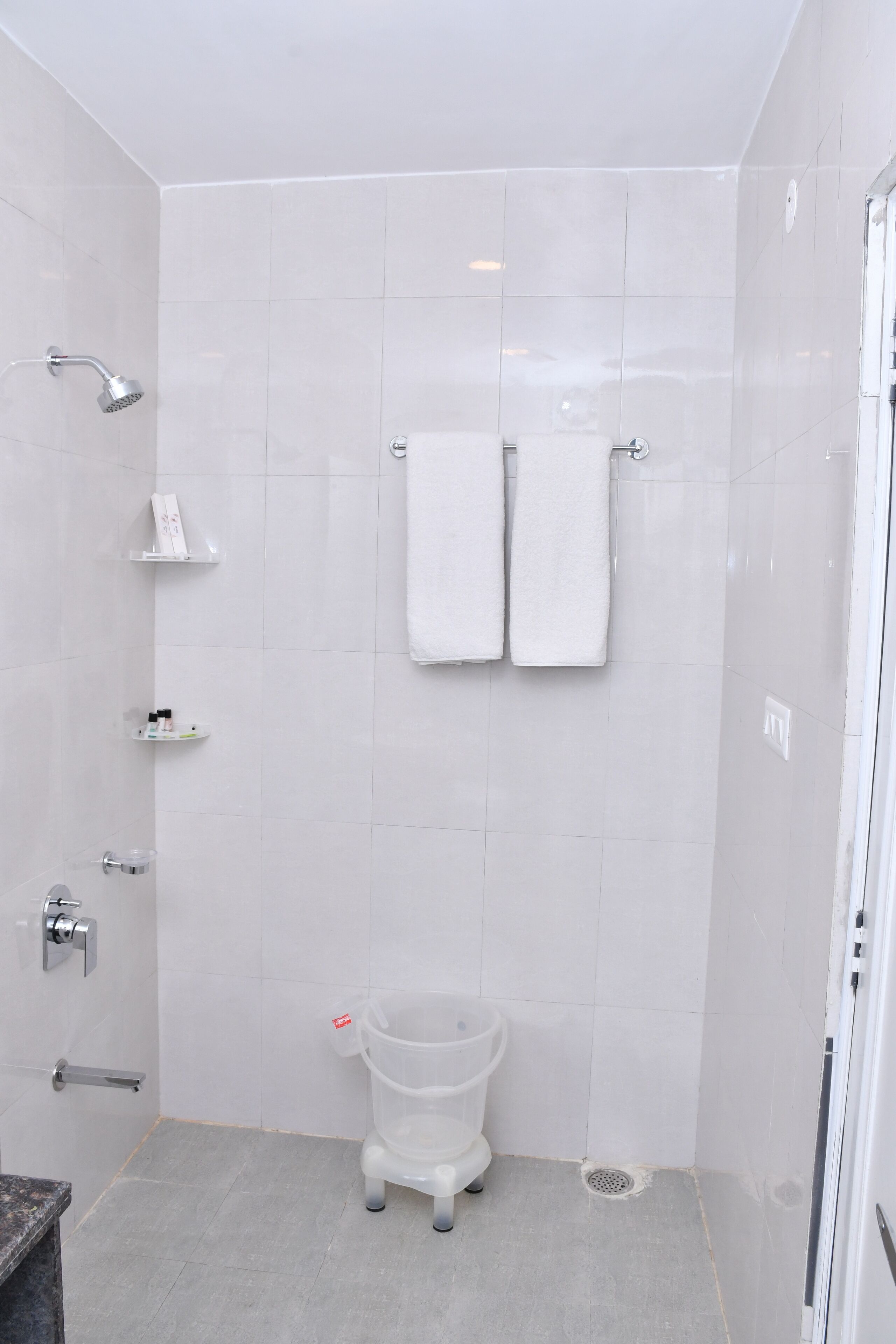 Un baño pequeño y moderno con azulejos blancos, ducha, inodoro y lavamanos. Hay dos toallas blancas colgadas en la pared.