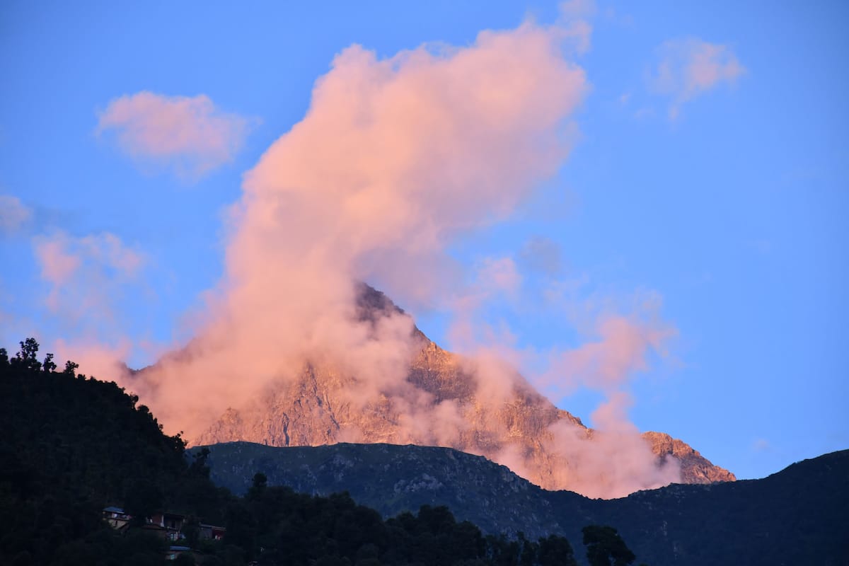 A mountain with a prominent peak, surrounded by clouds and a clear sky.