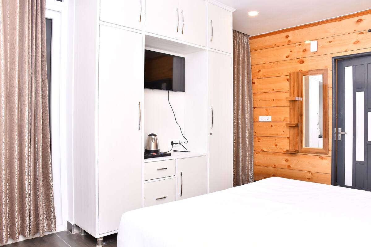 A bedroom with a bed, a white wardrobe, a television, and a wooden wall.