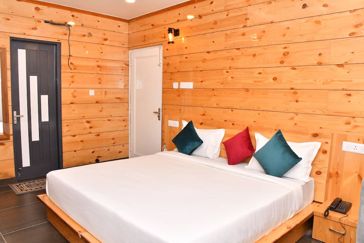 A wooden-paneled room with a bed, a door, and a bedside table with a phone.